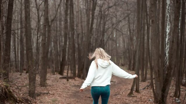 A happy blonde girl runs through the forest with her arms