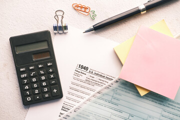 a Tax return form, calculator, paper and pen on table.