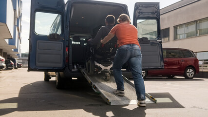 Assistant helping disabled person on wheelchair with transport using accessible vehicle ramp