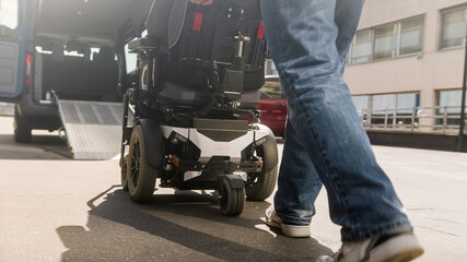 Assistant helping disabled person on wheelchair with transport using accessible vehicle ramp