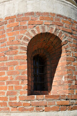 Fototapeta na wymiar Small window in an old brick wall. Vaulted window with iron bars. The shade from the sun on the window.