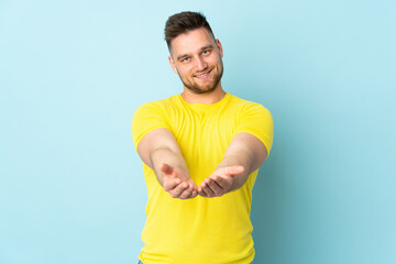 Russian handsome man isolated on blue background holding copyspace imaginary on the palm to insert...