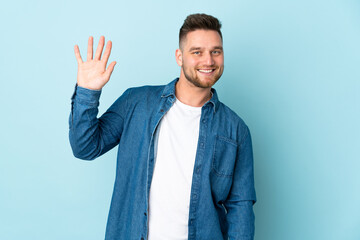 Russian handsome man isolated on blue background saluting with hand with happy expression