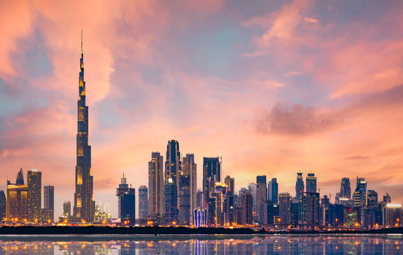 Stunning panoramic view of the illuminated Dubai skyline during a beautiful sunset. Silky smooth water flowing in the foreground. Dubai, United Arab Emirates.
