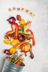 Peeled vegetables in compost bin and letters on concrete background. Top view. Recycling scarps...