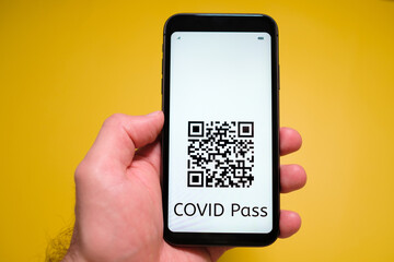 A smartphone with electronic immune digital health passport, Covid pass with QR code in mans hand on the yellow background.