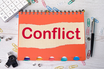 Conflict of interest, text on a piece of paper lying on a notebook on a desk next to a calculator, a flash drive, a pen and scattered paper clips.