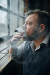 Man at the windowsill and smokes a cigar