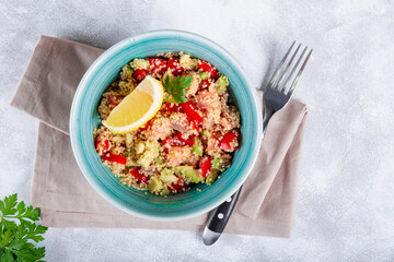  Salmon salad with tomatoes, avocado and quinoa in a blue bowl on a light gray table, a dish of balanced nutrition top view