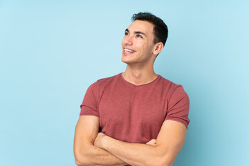 Obraz premium Young caucasian handsome man isolated on blue background looking up while smiling