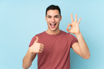 Fototapeta premium Young caucasian handsome man isolated on blue background showing ok sign and thumb up gesture