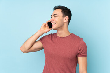 Young caucasian handsome man isolated on blue background keeping a conversation with the mobile phone