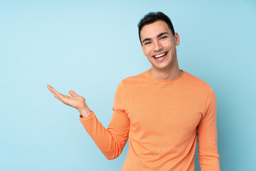 Young caucasian handsome man isolated on blue background holding copyspace imaginary on the palm to...