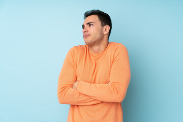 Young caucasian handsome man isolated on blue background making doubts gesture while lifting the shoulders