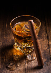 Single malt scotch whiskey in modern crystal glass with ice cubes and cuban cigar on wooden background