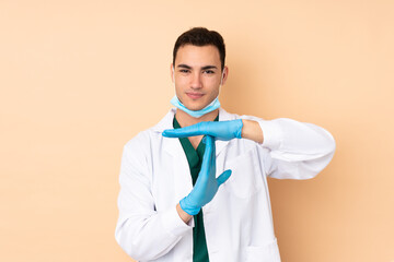 Young dentist man holding tools isolated on beige background making time out gesture