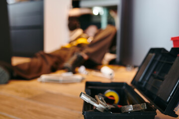 Toolbox with repairment handtools against plumber repairing kitchen sink