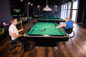 Adult men with disabilities in a wheelchair play billiards in the club