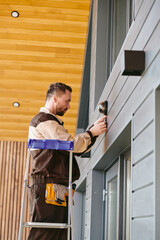 Young man fixing alarm system on wall above the door of living-room while standing on stepladder