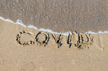 covid text on the sand on the beach. Waves from the sea erase the covid text.Removal of tourism restrictions in summer, opening of beaches. Covid free, safe beach, vaccine.Covid immunity passport