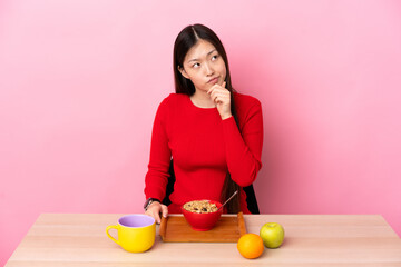 Young Chinese girl  having breakfast in a table having doubts