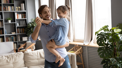 Happy loving young Caucasian father dance with cute little daughter in cozy living room on family...