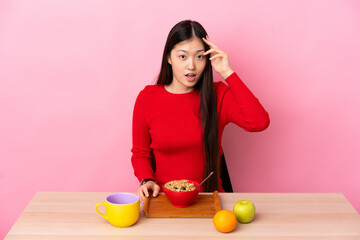Young Chinese girl  having breakfast in a table has realized something and intending the solution
