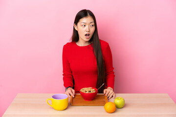 Young Chinese girl  having breakfast in a table doing surprise gesture while looking to the side