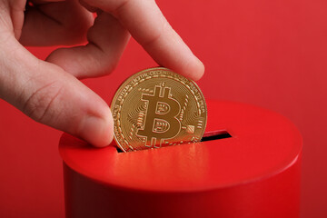 Men hand puts gold coin with bitcoin symbol into slot of red donation box. Concept crypto currency....