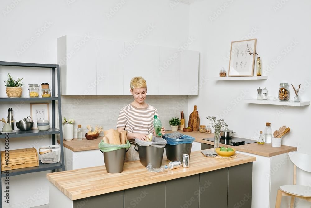 Sticker young female standing by kitchen table while sorting waste