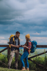 Couple of young hikers using a smartphone while wearing backpacks and a camping gear