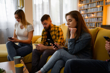 Friends hanging out on a house party while using smartphones and ignoring each other - obrazy, fototapety, plakaty