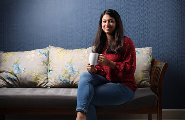 Young asian or indian girl drinking coffee on a sofa at home