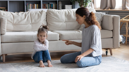 Strict young Caucasian mother talk lecture ill-behaved stubborn small preschooler daughter at home....