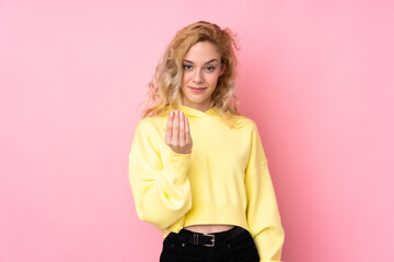 Young blonde woman wearing a sweatshirt isolated on pink background inviting to come with hand....