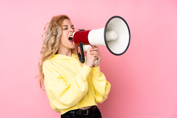 Young blonde woman wearing a sweatshirt isolated on pink background shouting through a megaphone - obrazy, fototapety, plakaty