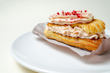Eclair with cream and strawberries. On a white plate High quality photo