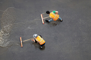Two workers cleans the street after the rain. Janitors with brushes washes wet city road, view from...