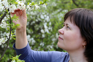 Obraz premium Young woman enjoys the smell of cherry blossom. White flowers in spring garden, romantic portrait of happy female inspired by nature, concept of happiness and romance