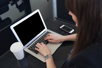 Woman working on laptop computer in the office. Focus on empty blank screen monitor.