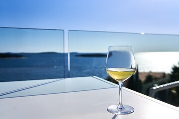 Glass of white wine on table on the terrace with the sea in the background. Summer vacation.