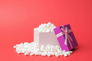 An open gift box overflowing with marshmallows on a red background.