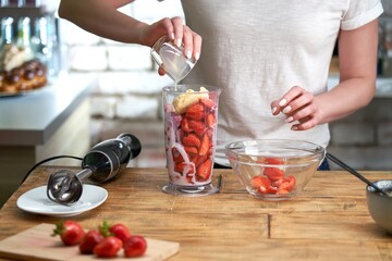 Woman making strawberry smoothie. Healthy eating, cooking and summer refreshment concepts.