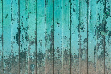 Fragment of an old green fence made of profiled sheet. There is corrosion in the lower part, the paint has collapsed and crumbled. Background. Texture.