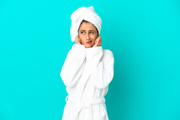 Young woman in a bathrobe over isolated blue background frustrated and covering ears