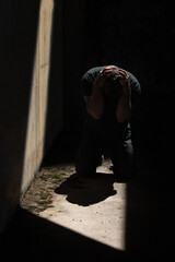 Man kneeling and holding his head with his hands, depressed and desperate in darkness with one...
