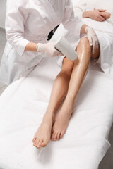 Obraz na płótnie Canvas Depilation and beauty spa clinic concept. Close up of women legs getting laser hair removal treatment at cosmetology salon, doctor depilating leg with hardware cosmetic device