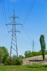 Obraz premium Power line pylons surrounded with greenery and trees with bright blue sky
