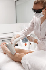 Vertical shot of beautician depilation master using laser for legs hair removal procedure at beauty clinic, cosmetologist wears protective glasses, use device on leg covered soothing cosmetic gel