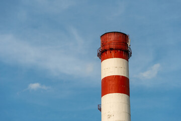 A large industrial smokestack against a blue sky. Red and white pipe in commercial enterprises or power plants.